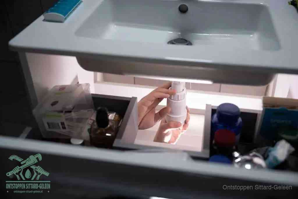 Een pompfles met zeep boven een wastafel, de heet water en afwasmiddel-methode om een vetprop in de afvoer los te maken in Sittard-Geleen