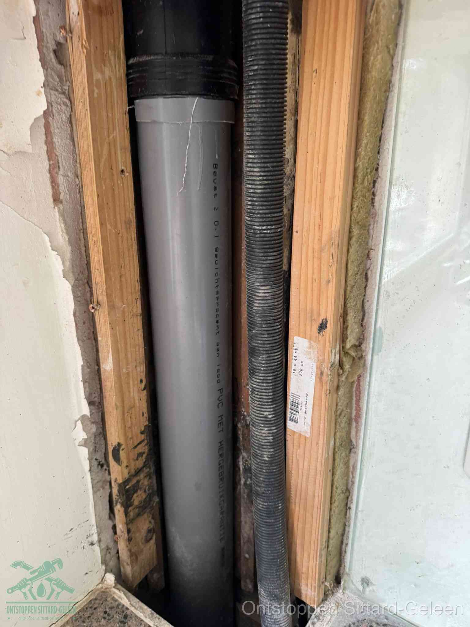 Een grijze PVC-afvoerbuis met een flexibele ribbelslang in een open wandconstructie, een verwaarloosde afvoer die te lang is blijven zitten in Sittard-Geleen