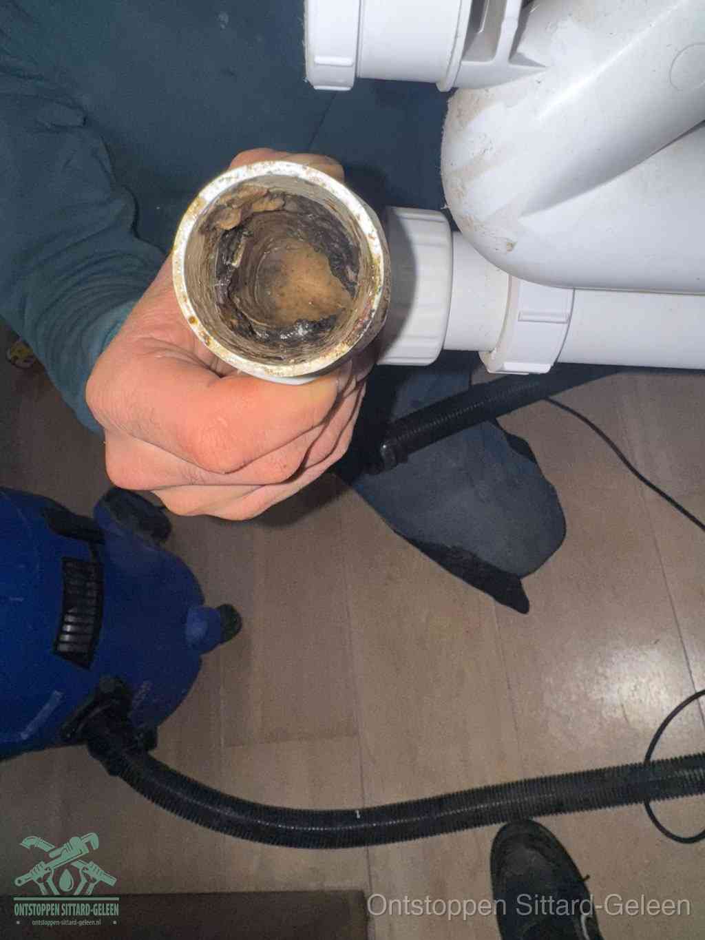 Een hand houdt een losgekoppeld PVC-afvoerbuisstuk vast dat van binnen volledig is dichtgeslibd met vet, vuil en aanslag, de meest voorkomende oorzaak van een verstopte afvoer in Sittard-Geleen