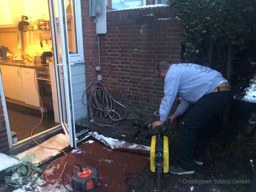 Een monteur werkt buiten bij een open riool-/grondput met een elektrische ontstoppingsmachine om een verborgen afvoerprobleem op te sporen in Sittard-Geleen