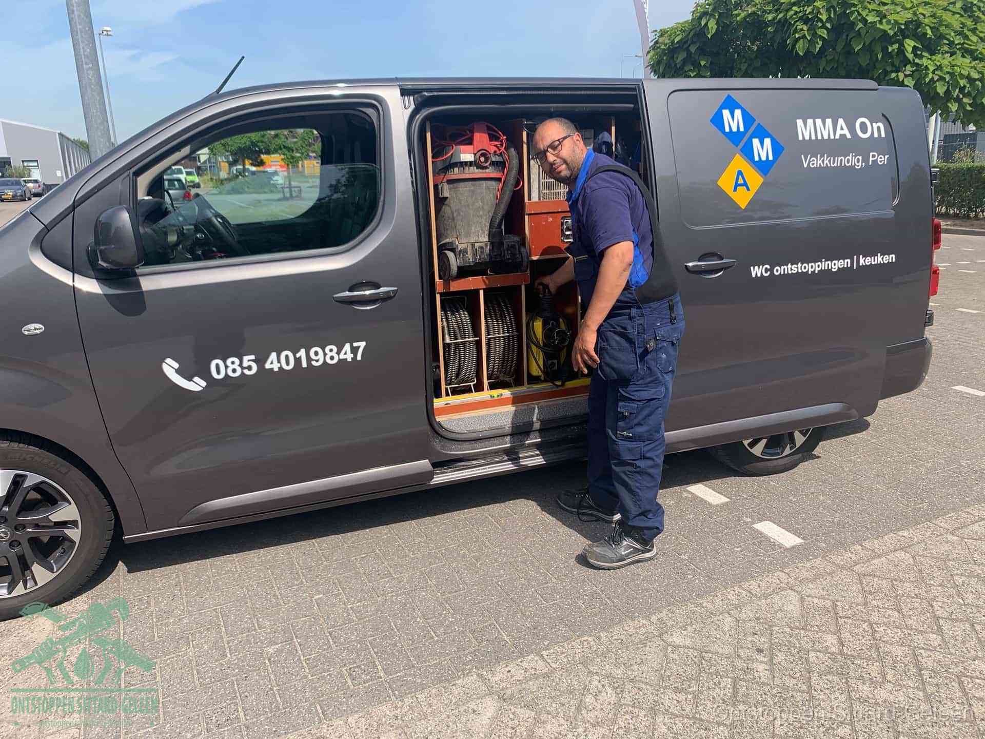 Een monteur bij de open schuifdeur van zijn bedrijfsbus op een parkeerplaats, klaar om de oorzaak van terugkerende afvoerverstoppingen aan te pakken in Sittard-Geleen
