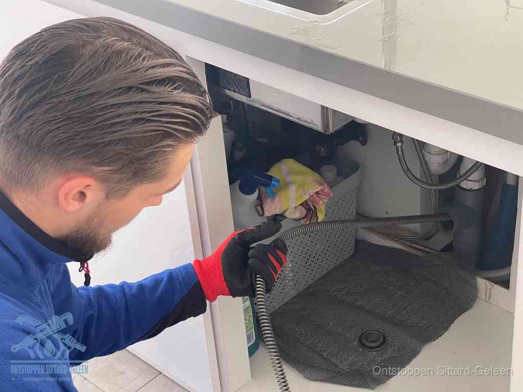 Een monteur voert een flexibele ontstoppingsveer in de afvoer om een verstopping voorbij de bocht van het toilet te bereiken in Sittard-Geleen