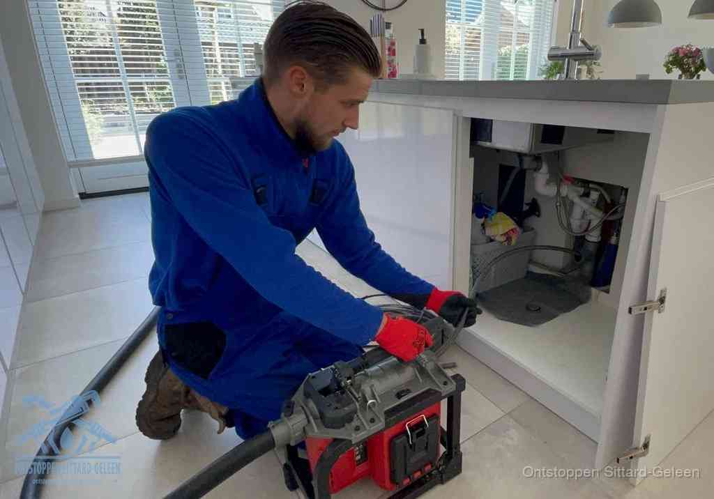 Een monteur voert een professionele elektrische ontstoppingsmachine in de afvoer onder de spoelbak tijdens het gootsteen ontstoppen in Sittard-Geleen