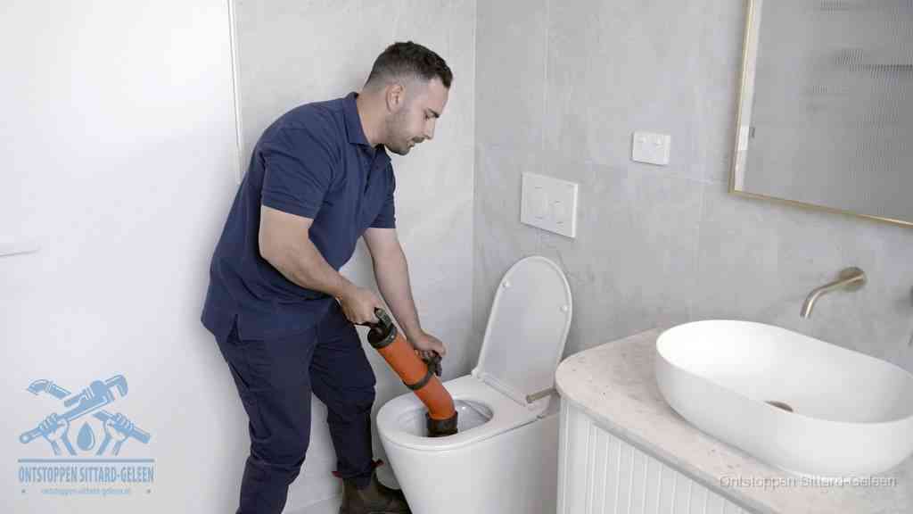 Een man gebruikt een handmatige luchtdruk-ontstopper in een modern betegeld toilet om zelf de wc te ontstoppen in Sittard-Geleen
